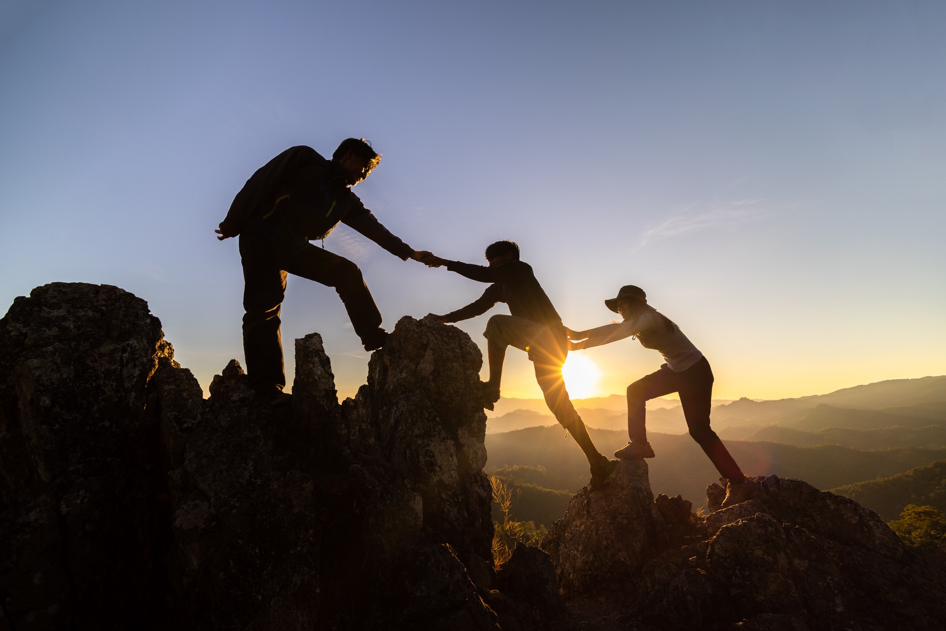 silhouette of Teamwork of three  hiker helping each other on top of mountain climbing team. Teamwork friendship hiking help each other trust assistance silhouette in mountains, sunrise.